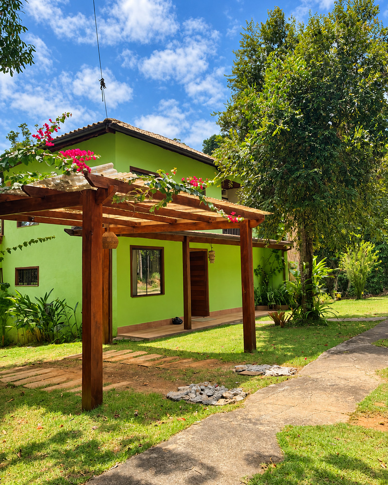Fachada verde da Casa Verde com pérgola de madeira e jardim
