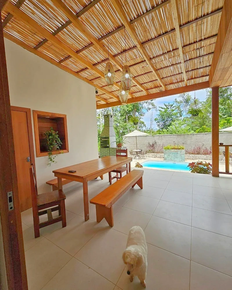 Varanda coberta com mesa, piscina e vegetação ao redor